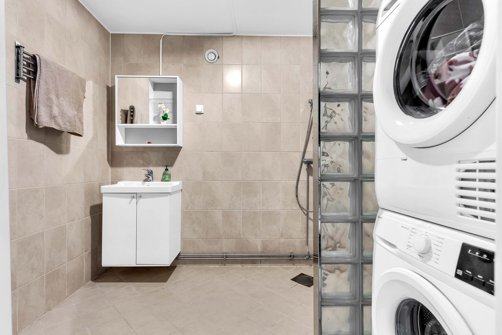 Flislagt baderom fra byggeåret med baderomsinnredning bestående av vegghengt servantskap, servant, speilskap og dusj på gulv med glassvegg. Galleribilde