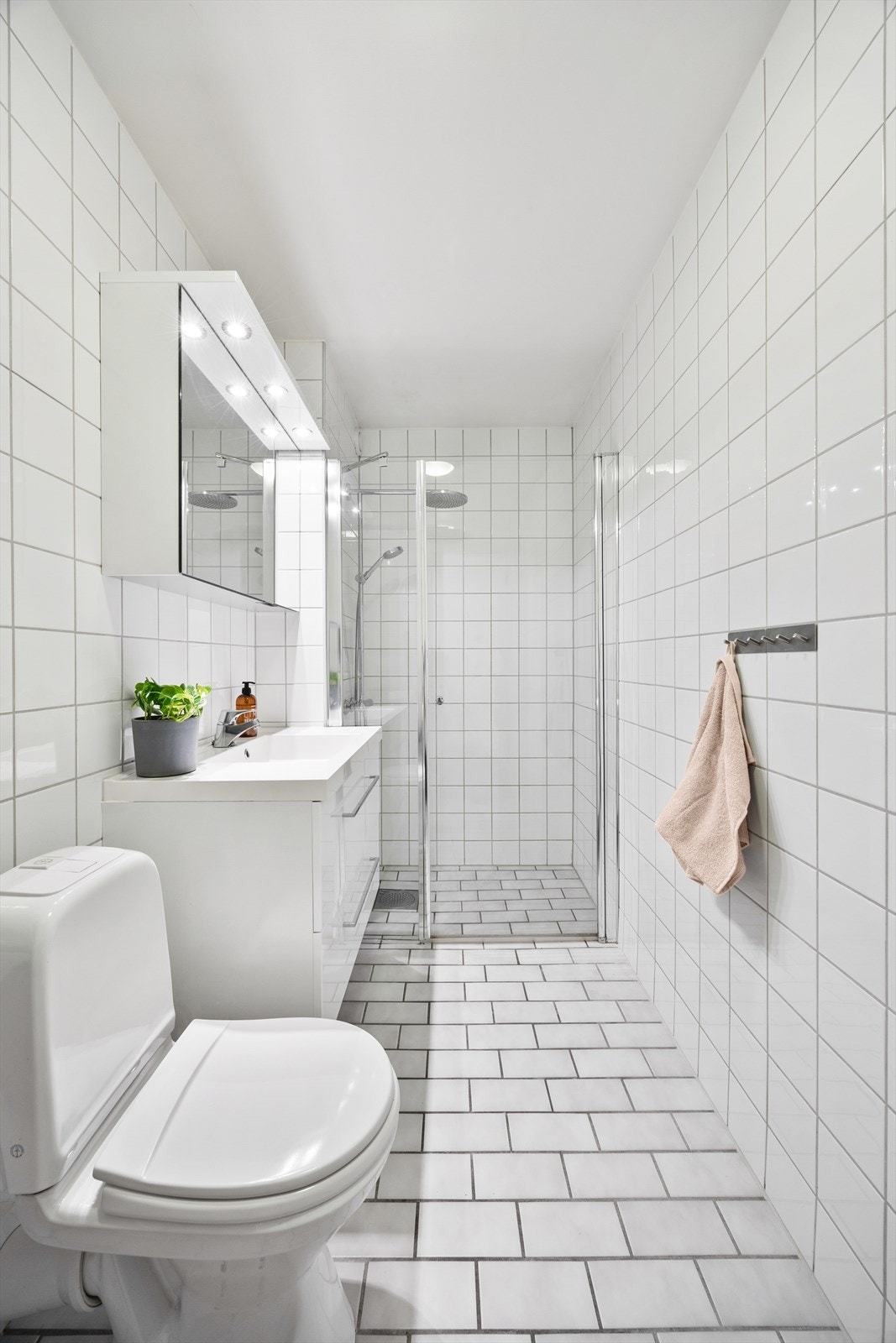 Innredningen inkluderer et benkeskap med glatte fronter, servant, klosett og en praktisk dusjnisje med dør i herdet glass Galleribilde