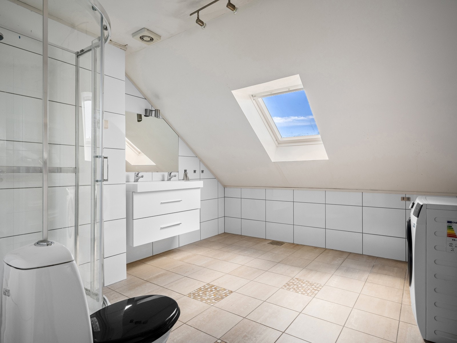 Badet er innredet med baderomsinnredning med dobbel vask, dusjkabinett, toalett og opplegg for vaskemaskin Galleribilde