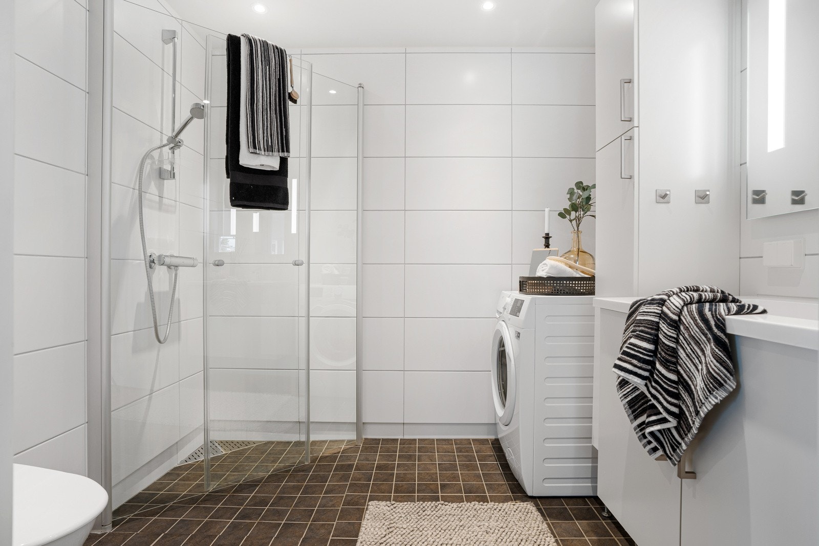 Leilighetens bad er stilrent innredet med en servant med romslig skuffeinnredning, dusjhjørne m/innfellbare glassdører, speil med integrert lys, wc og opplegg for vaskemaskin. Galleribilde