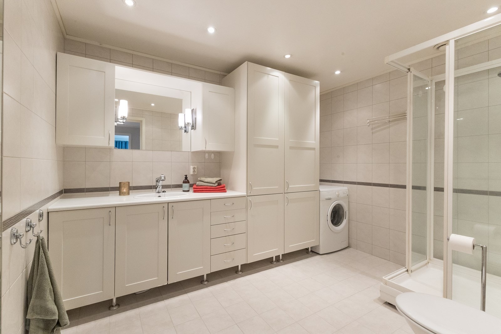 Her er det flis på gulv og vegger. Badet er romslig og har innredning med nedfelt servant, veggmontert toalett med innebygget sisterne, dusjkabinett og opplegg for vaskemaskin. Galleribilde