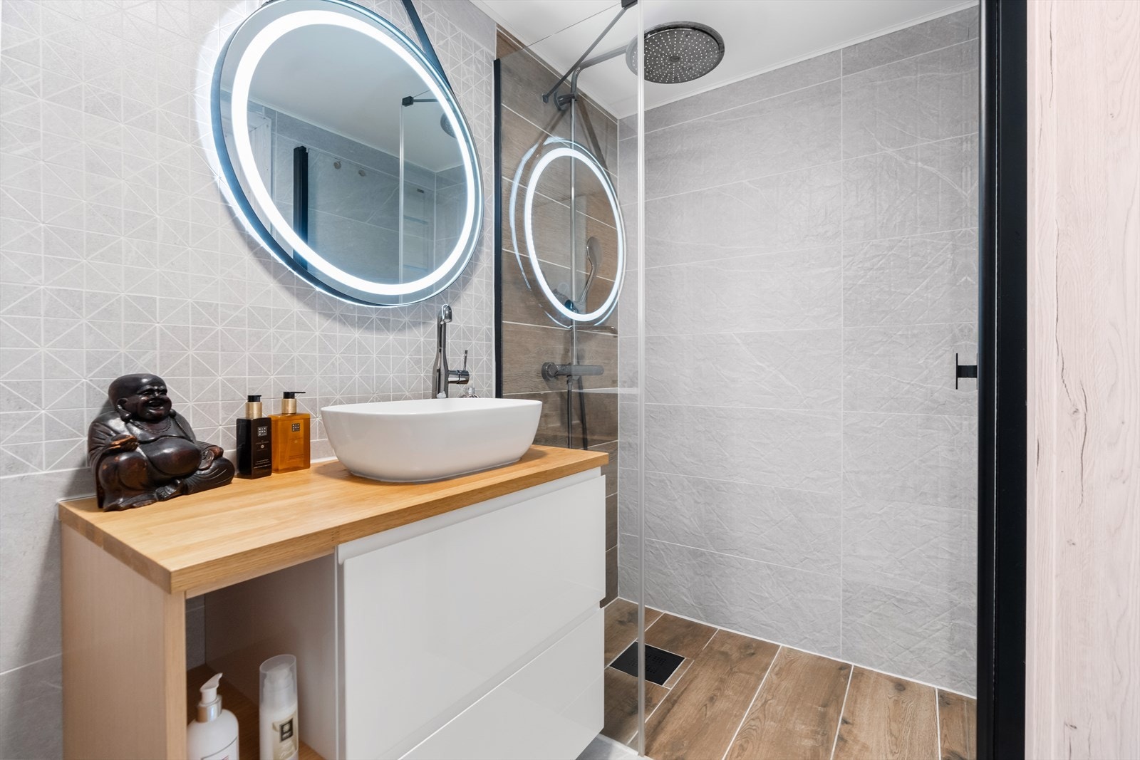 Badet inneholder innredning med lys, vegghengt toalett og dusj i hjørne bak glassvegger. Galleribilde