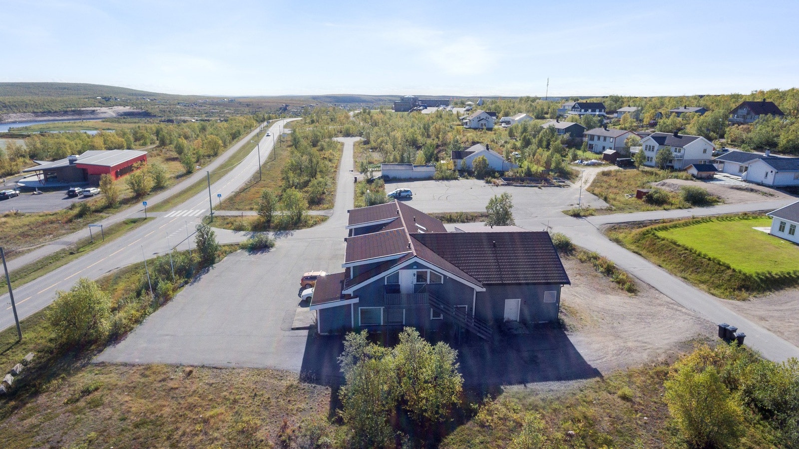 Dronebilde mot sør. Thon Hotel i bakgrunn. Området rundt eiendommen er spredt bolig bebyggelse. Galleribilde