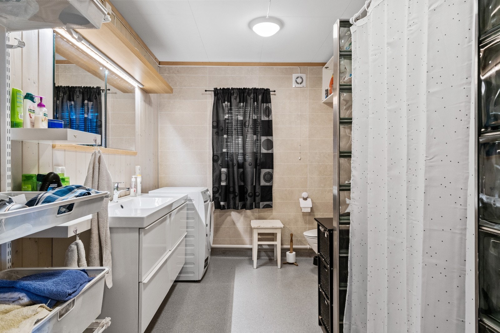 Badet er innredet med servantskap med heldekkende servantplate, stort speil, gulvmontert toalett samt dusjnisje med glassbyggerstein og forheng. Opplegg for vaskemaskin. Galleribilde