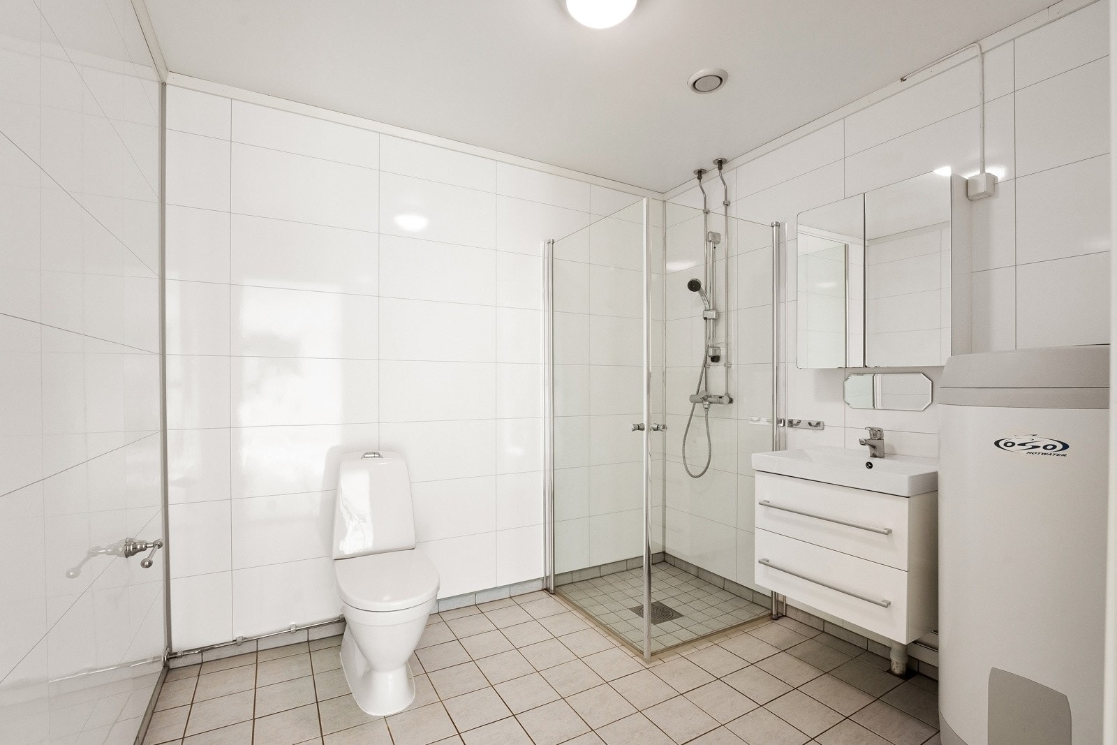 Stort bad med stilrene fliser på gulv på vegger. Badet har servant innredning som har godt med skuffplass, wc og dusjhjørne med vegger av herdet glass. Galleribilde