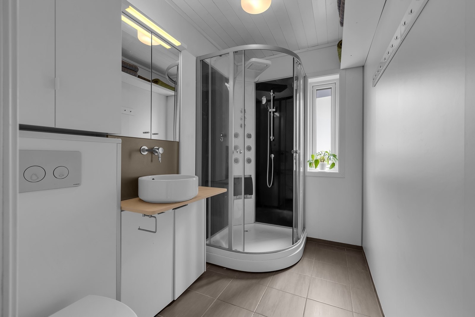 Baderom i 1. etasje med flis på gulv, dusjkabinett og vegghengt toalett. Galleribilde