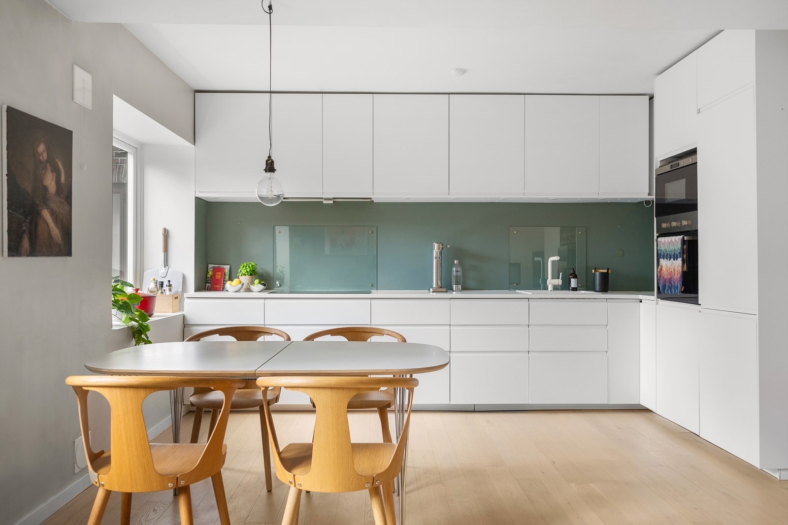 Innredning med hvite, glatte fronter og benkeplate i laminat. Glassplate på vegg over koketopp og oppvaskkum. Galleribilde