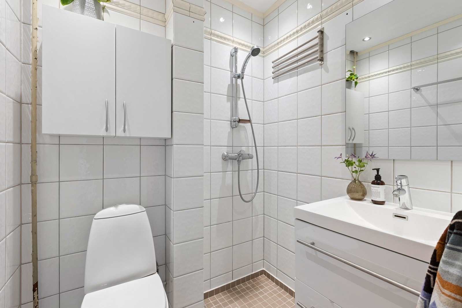 Flislagt bad som inneholder vegghengt innredning med heldekkende servant, speil, gulvmontert wc og dusjhjørne. Galleribilde