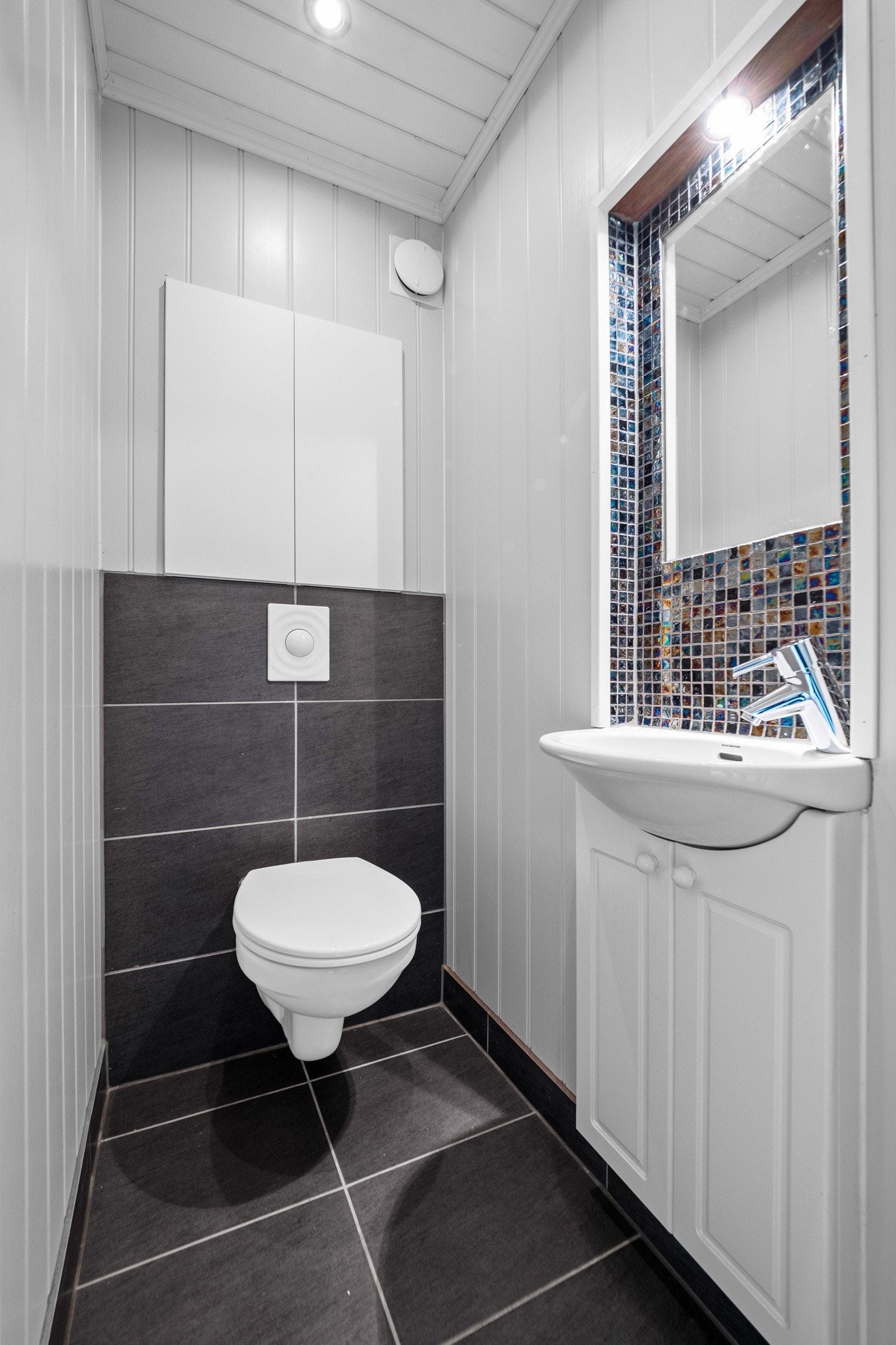 Vegg-i-vegg med badet ligger toalettrommet, pent utført med veggmontert toalett, gulvfliser og downlights. Galleribilde