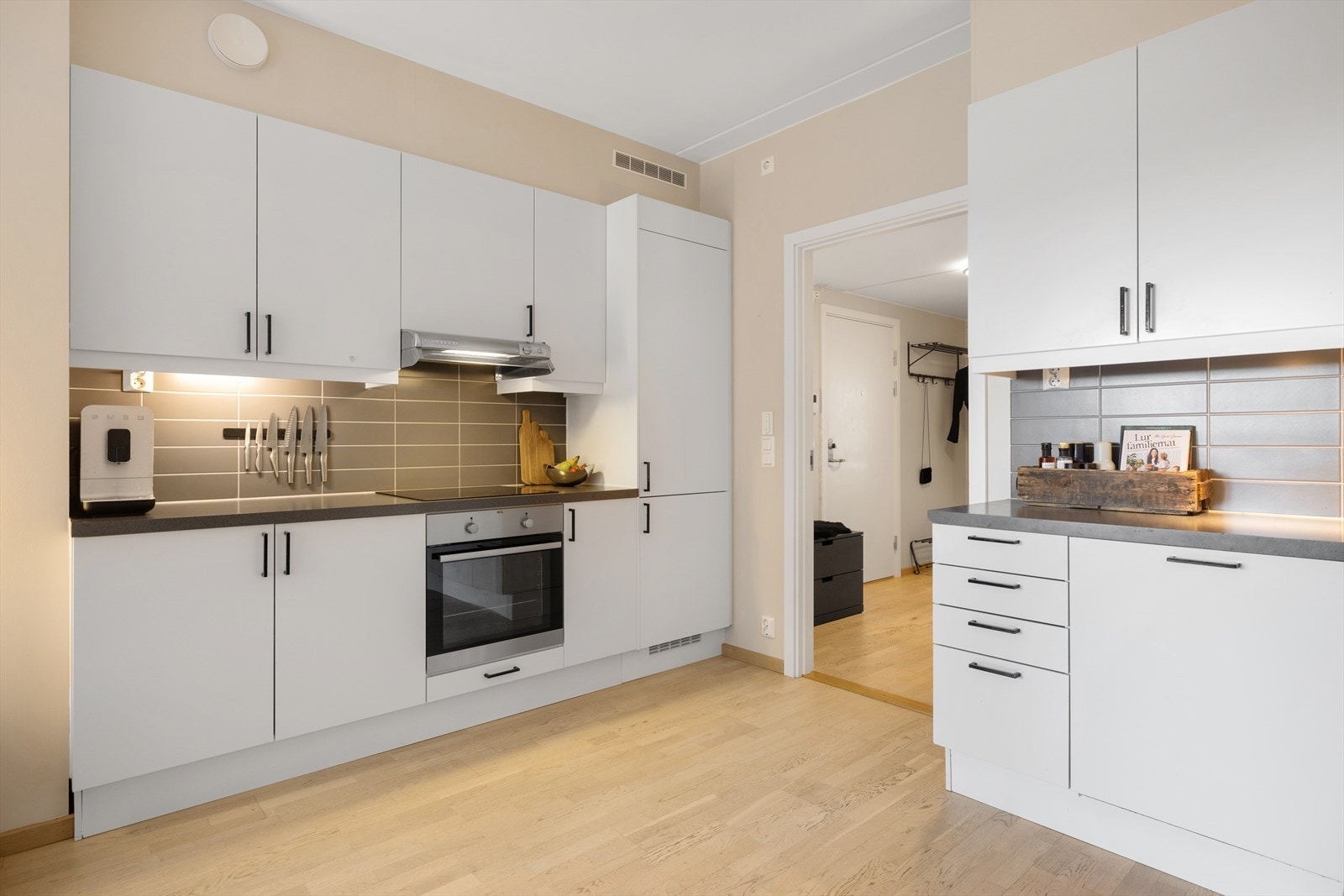 Innredningen har hvite matte fronter, benkeplater i laminat, rustfri oppvaskkum, ventilator og fliser over benkeskap. Galleribilde