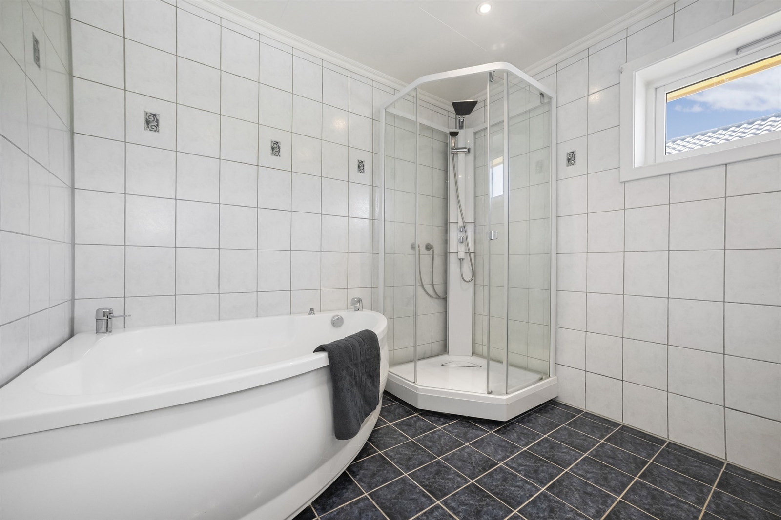 Badet er utstyrt med gulvstående toalett, servantskap og hjørnebadekar Galleribilde