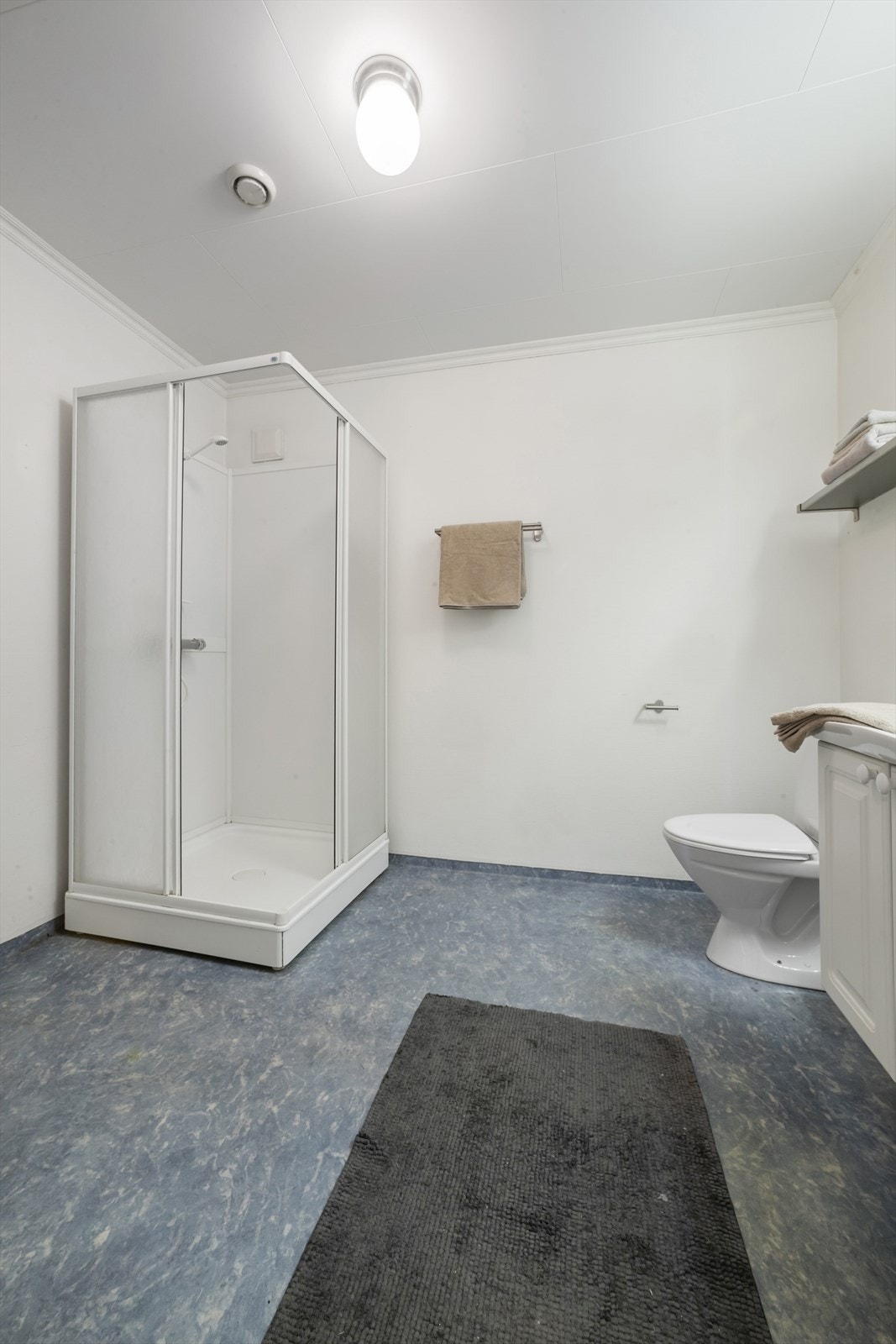 Badet har dusjkabinett, gulvstående toalett, servantskap og opplegg for vaskemaskin Galleribilde