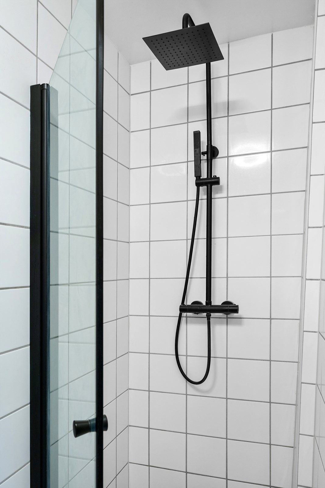Badet er utstyrt med en stilren regnfallsdusj og pen dusjdør med sorte detaljer. Galleribilde