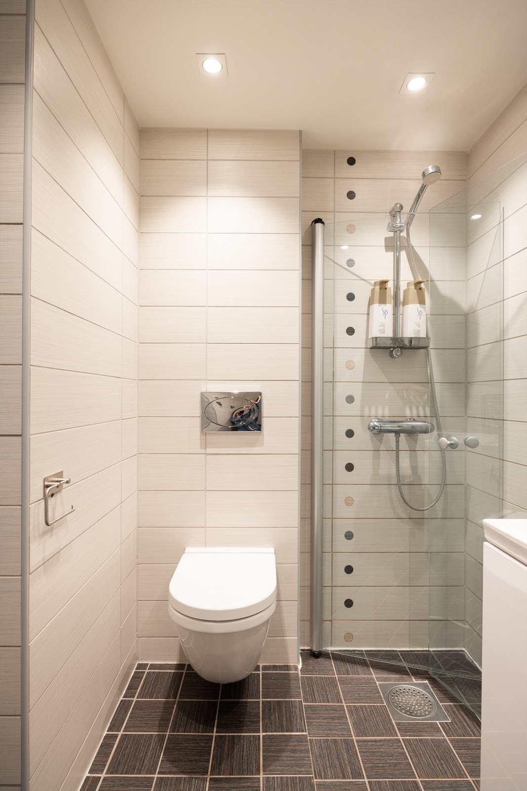 Badet er innredet med vegghengt klosett, servant nedfelt i innredning, speil og dusjhjørne med svingbare glassdører. Galleribilde