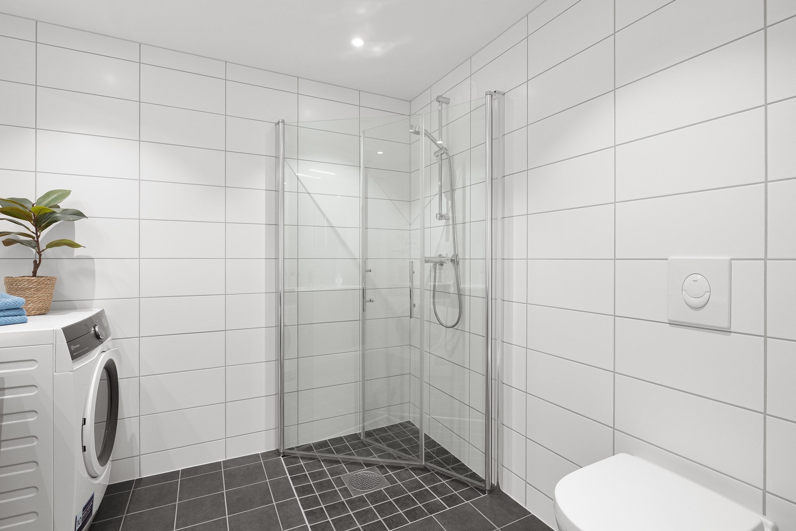 Videre er det dusj på gulv i hjørnet med innfellbare dusjdører og to-greps dusjarmatur. Galleribilde