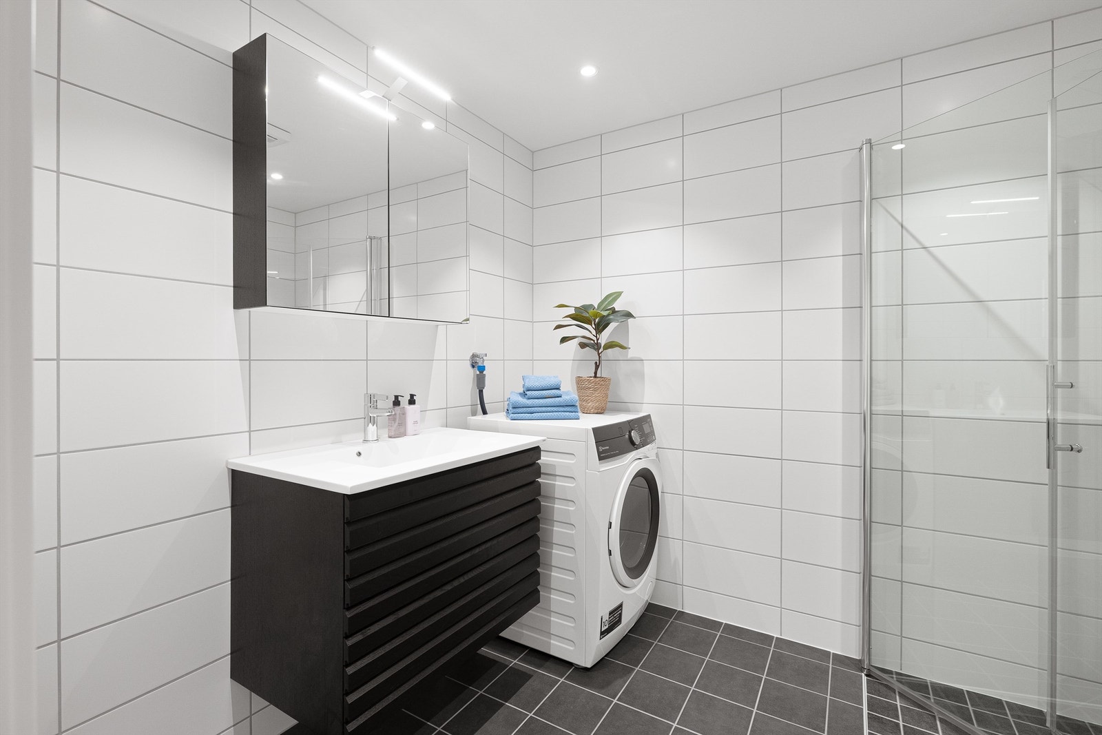 Delikat og tidløst baderom med varme i flislagt gulv. Flislagte vegger, himling med downlights og vegghengt innredning fra HTH Nordic Spirit. Galleribilde