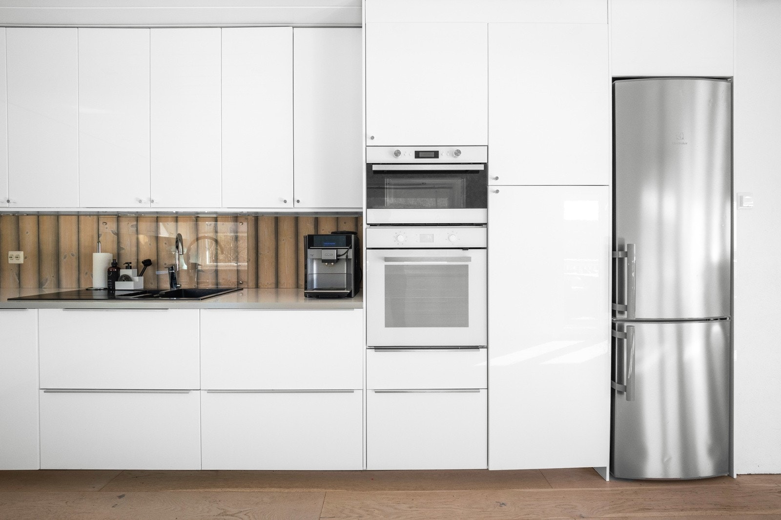 Integrert hvitevarer som stekeovn, mikrobølgeovn og platetopp, samt oppvaskmaskin i benk og frittstående kjøleskap i høyskap Galleribilde