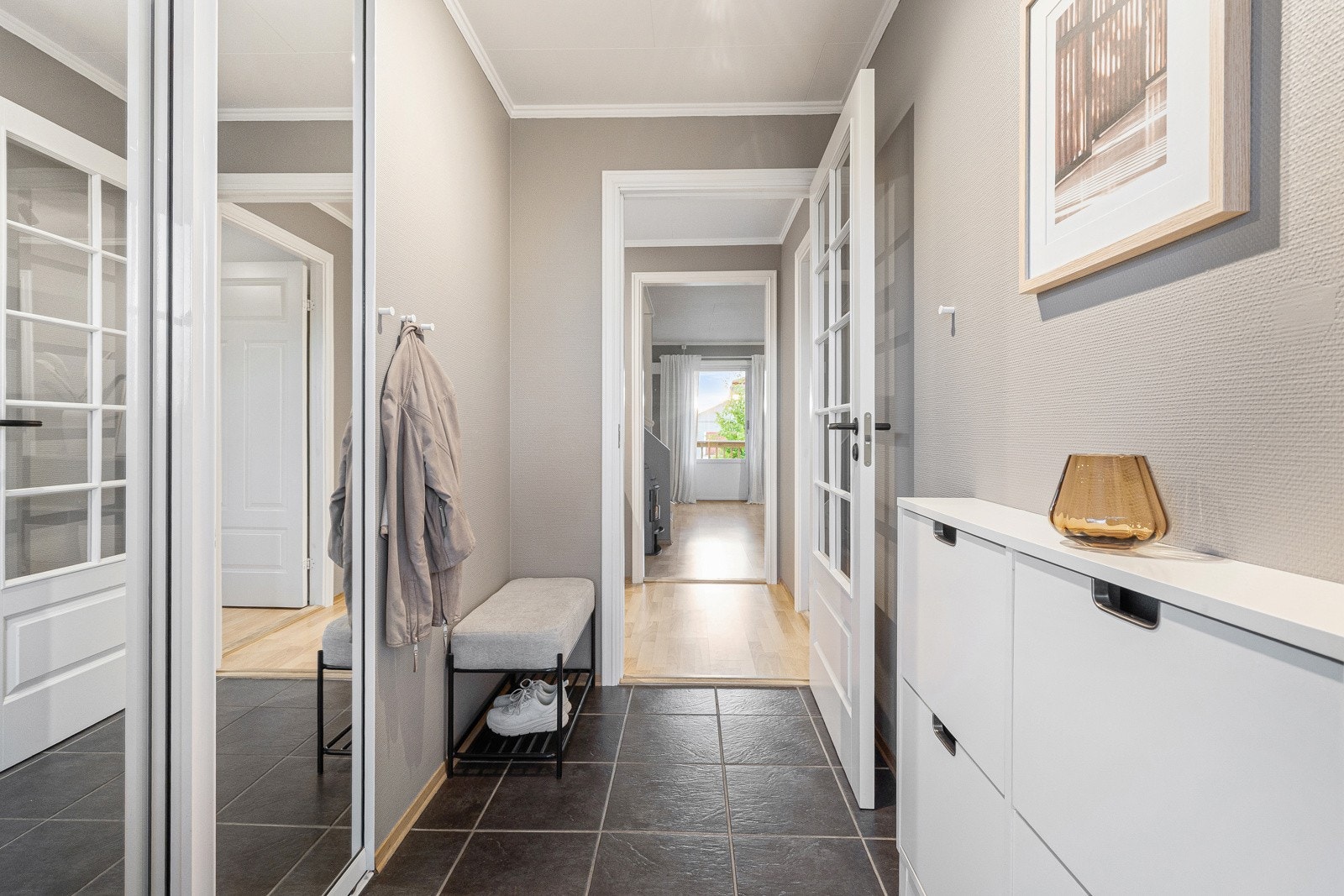 Innbydende entre med fliser på gulv med gulvvarme og lysmalte veggflater, som gir et godt førsteinntrykk av leiligheten. Det er satt inn en stilren skyvedørsgarderobe i egen nisje i vegg. Galleribilde