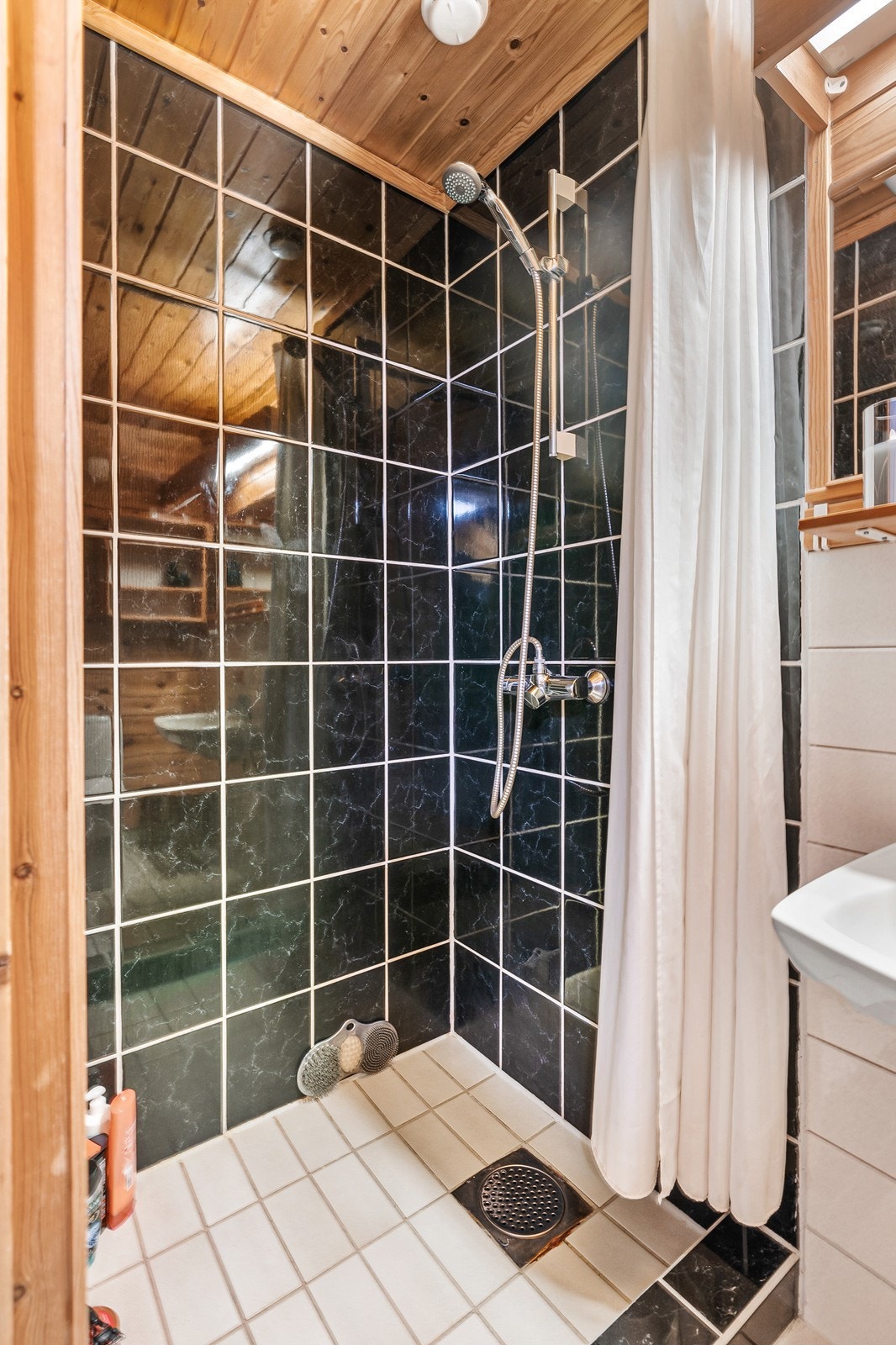 Videre er det innredet med vask, toalett og dusjhjørne med forheng. Badet er fra byggeår og fremstår med moderniseringsbehov. Galleribilde