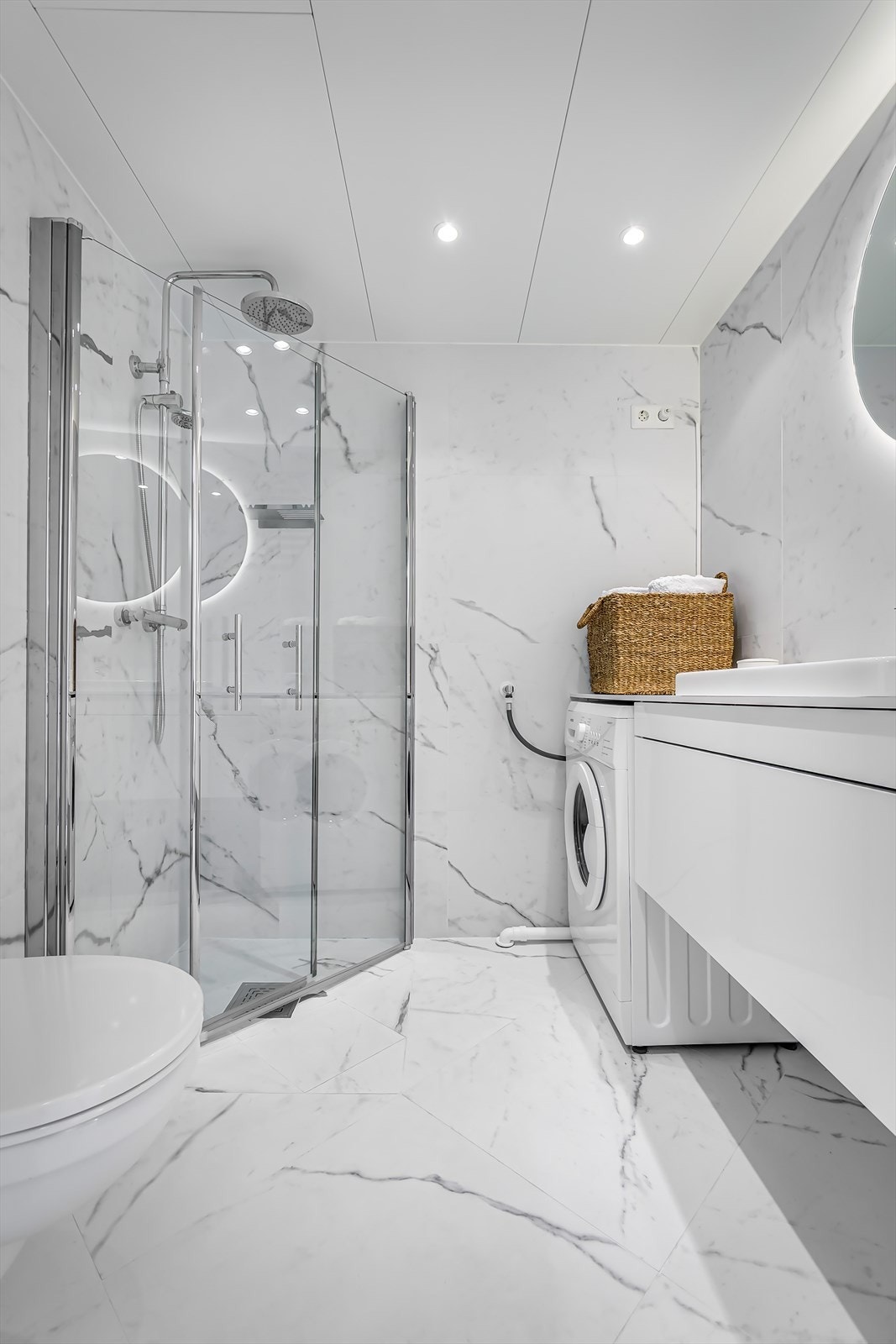 Badet er utstyrt med et dusjhjørne med glassdører, et veggmontert toalett, en servantinnredning samt opplegg for vaskemaskin. Galleribilde