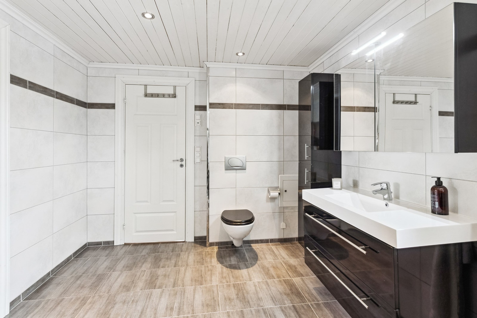 Det romslige badet har servant i innredning, vegghengt toalett og flislagt dusjnisje med glassdør Galleribilde