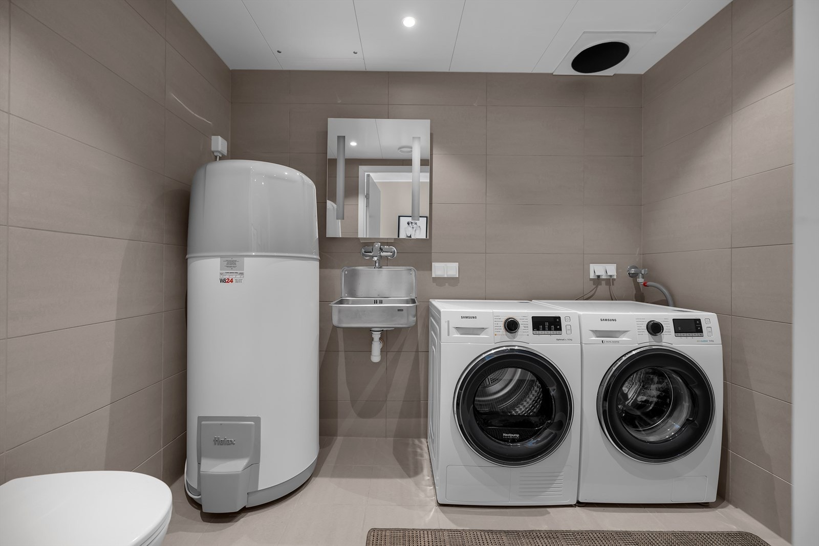 Moderne vaskerom med vaskemaskin, tørketrommel, skyllekar og varmtvannsbereder. Komplett flislagt. Praktisk og stilrent design. Montert ekstra WC i rommet. Galleribilde