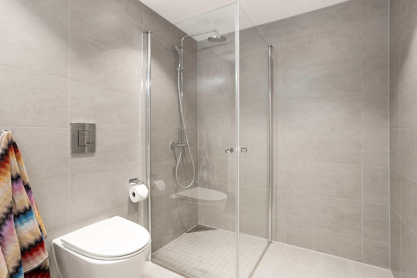 Dusj med innfellbare glassvegger og regnfallsdusjdusj. Vegghengt toalett. Galleribilde