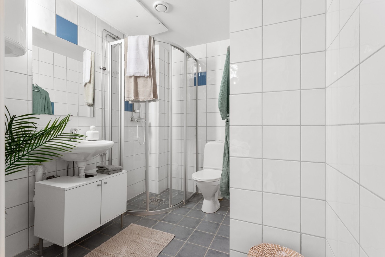 Flislagt bad med dusjhjørne, servant med innredning og opplegg for vaskemaskin. Galleribilde