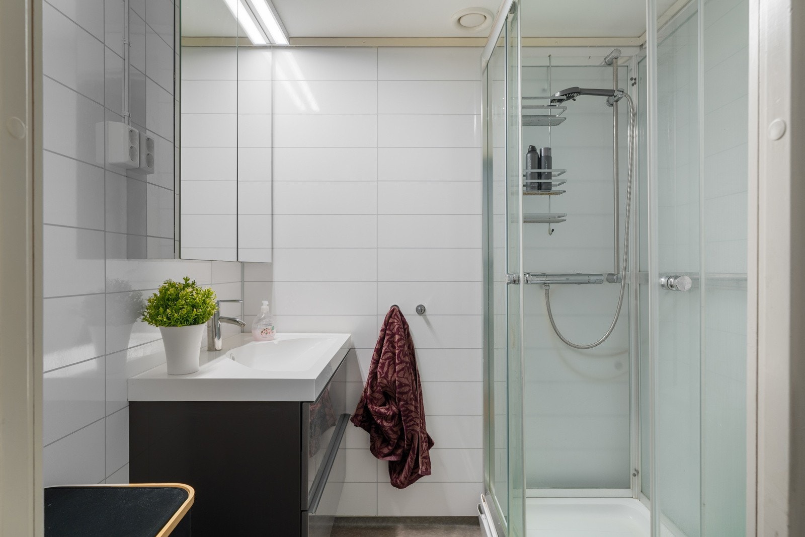 Lyst bad på hybelavdelingen med dusjkabinett og nyere servant med en pen innredning med speilskap for god oppbevaring. Galleribilde