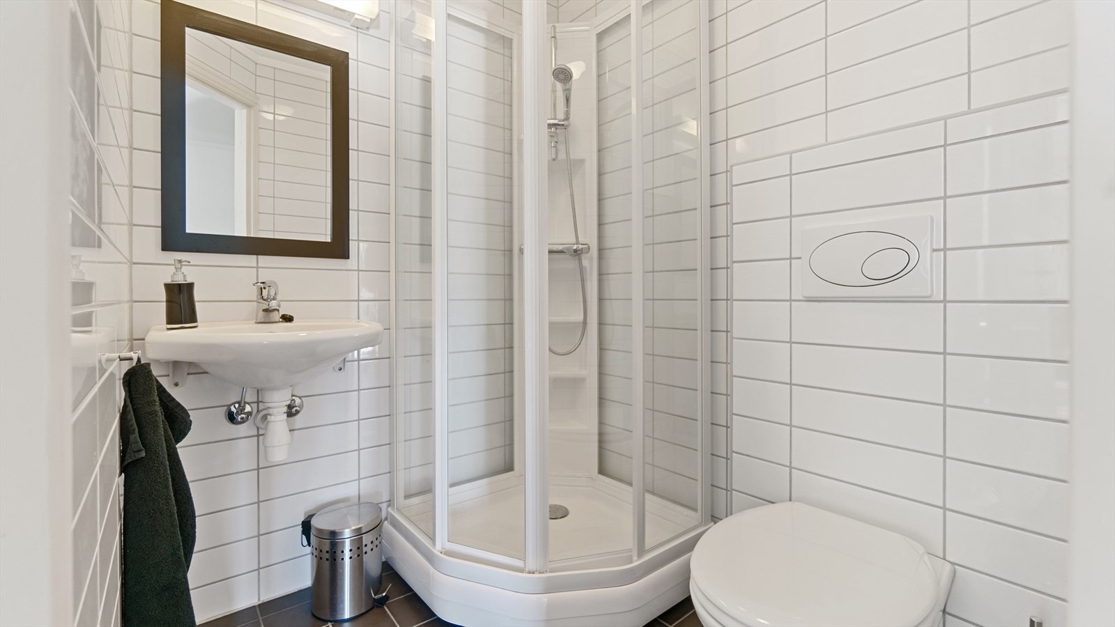 Flislagt baderom i kontorlokalet, med standard fra byggeår. Badet har veggmontert toalett, dusjkabinett og servant. Galleribilde