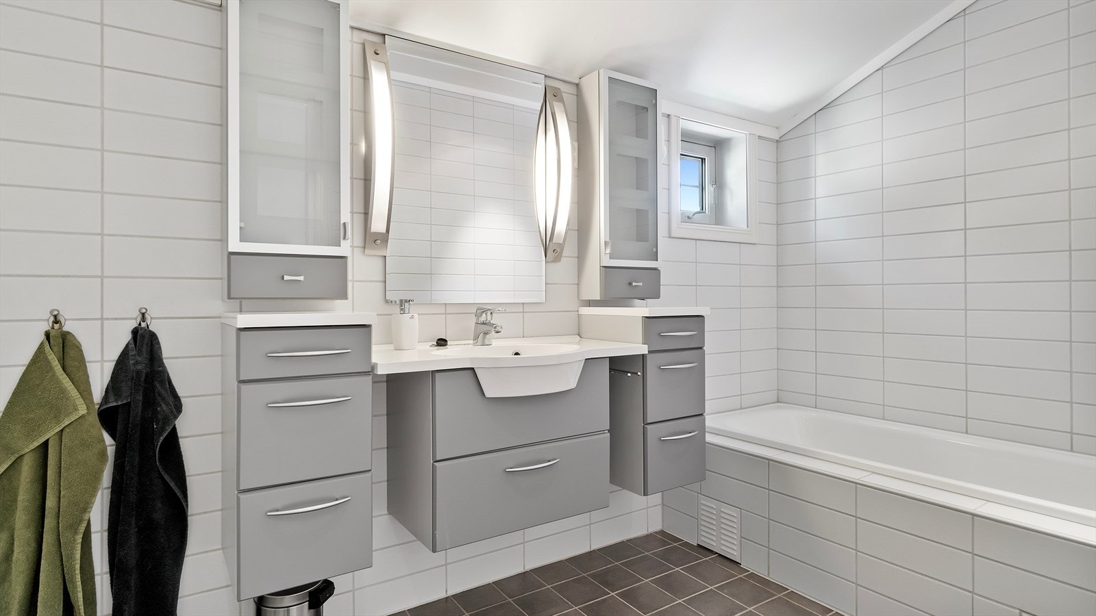 Lyst, flislagt baderom i 3. etasje, med standard fra byggeår. Badet har veggmontert toalett, dusjkabinett og innfliset badekar. Galleribilde