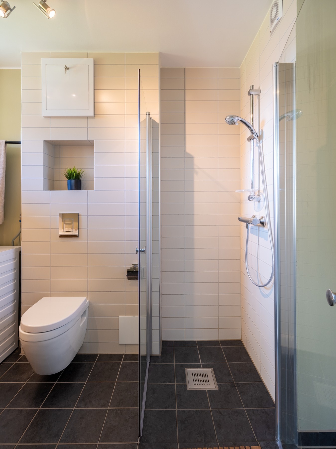 Videre er badet utstyrt med dusjhjørne med innfellbare glassdører og to-greps armatur påkoblet hånddusj, samt et vegghengt toalett. Galleribilde