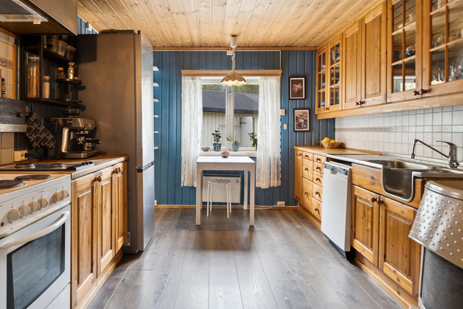 Kjøkkenet har blåmalt panel på veggene og laminat på gulvet. Kjøkkeninnredning på to vegger med profilerte fronter og laminerte benkeplater. Galleribilde