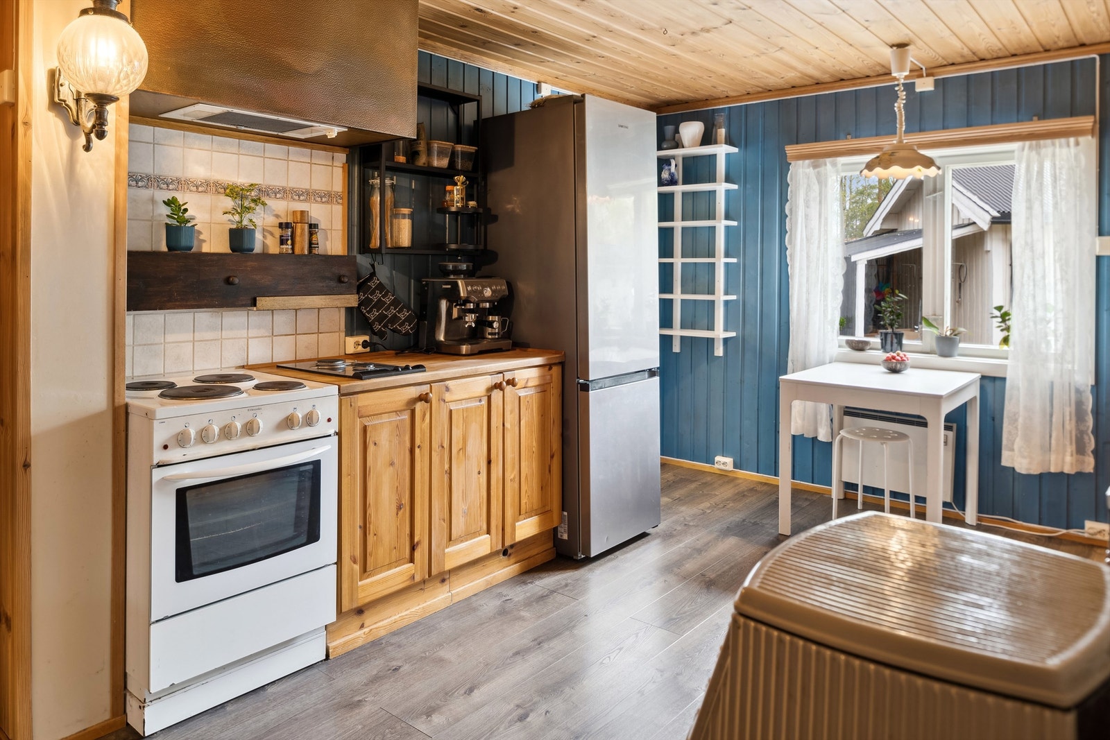 Kjøkkeninnredningen består av skuffer, underskap og overskap, to doble overskap med glassdører. Lyse og mønstrete fliser på veggflatene over kjøkkenbenkene. Galleribilde