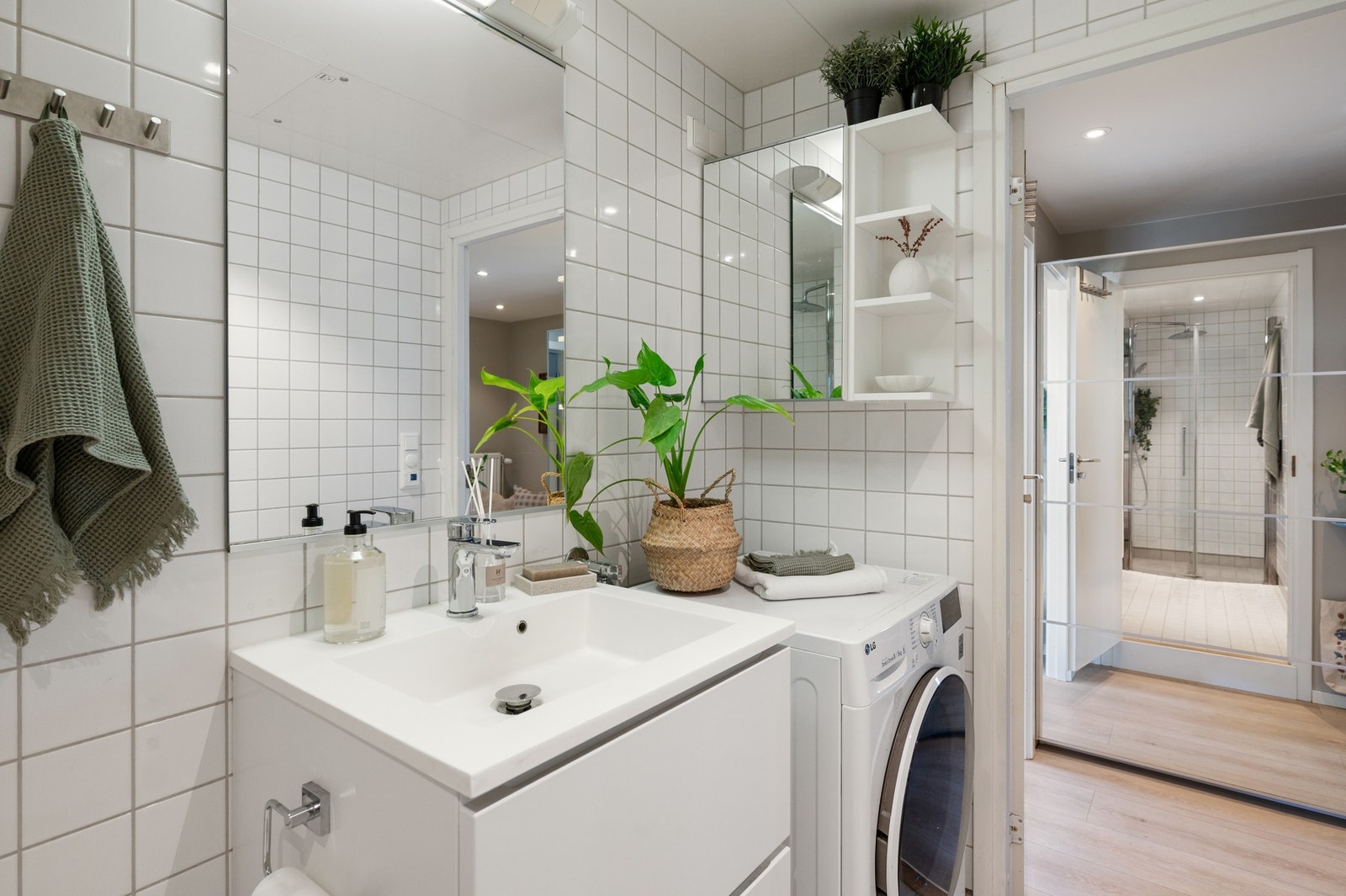 Lyst og moderne bad, innredet med hvite fliser, servant med skuffer og speil med lys over. Galleribilde