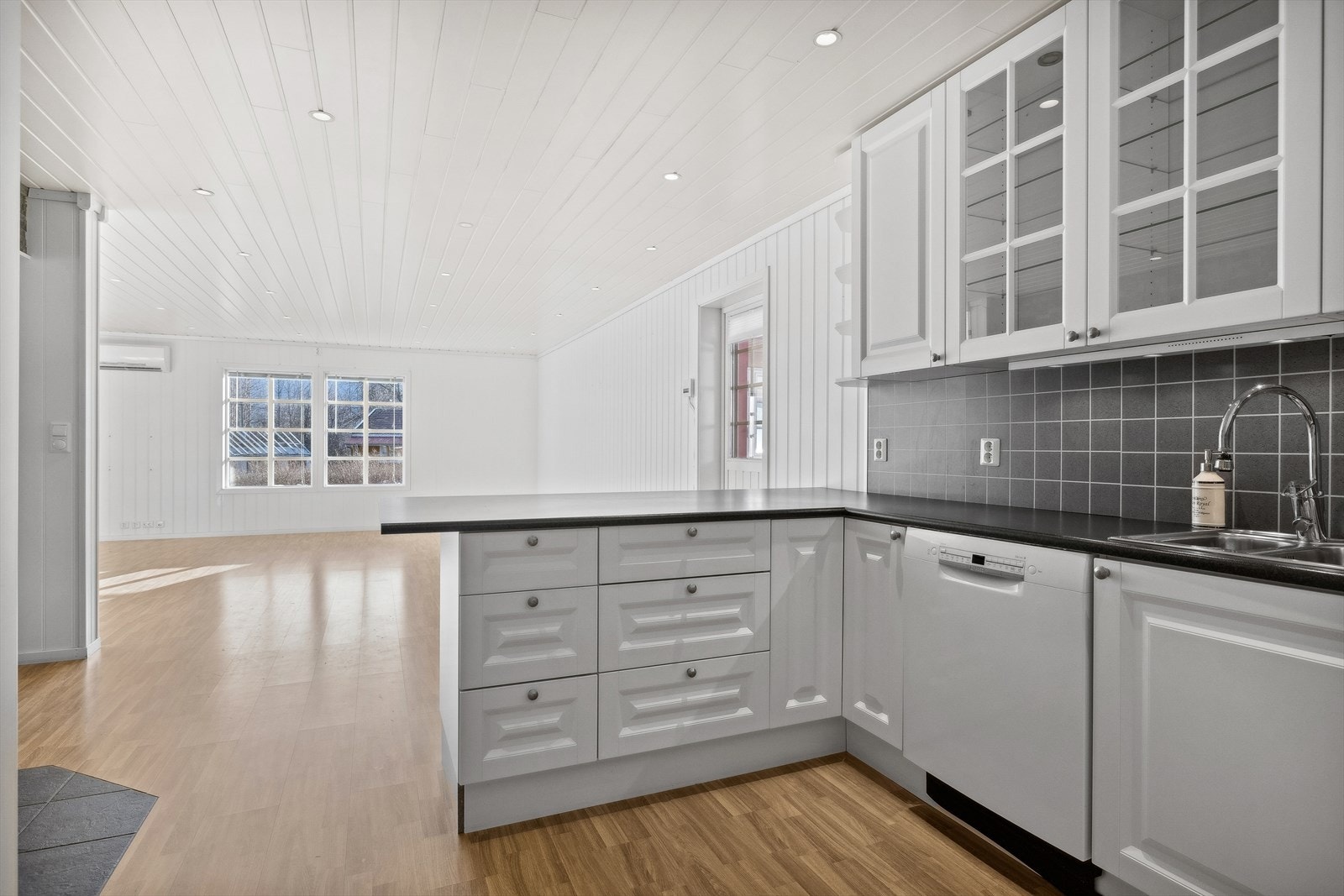 Åpen kjøkken løsning mot stue med nyere kjøkkeninnredning som har profilerte fronter og overskap med glassdører. Galleribilde