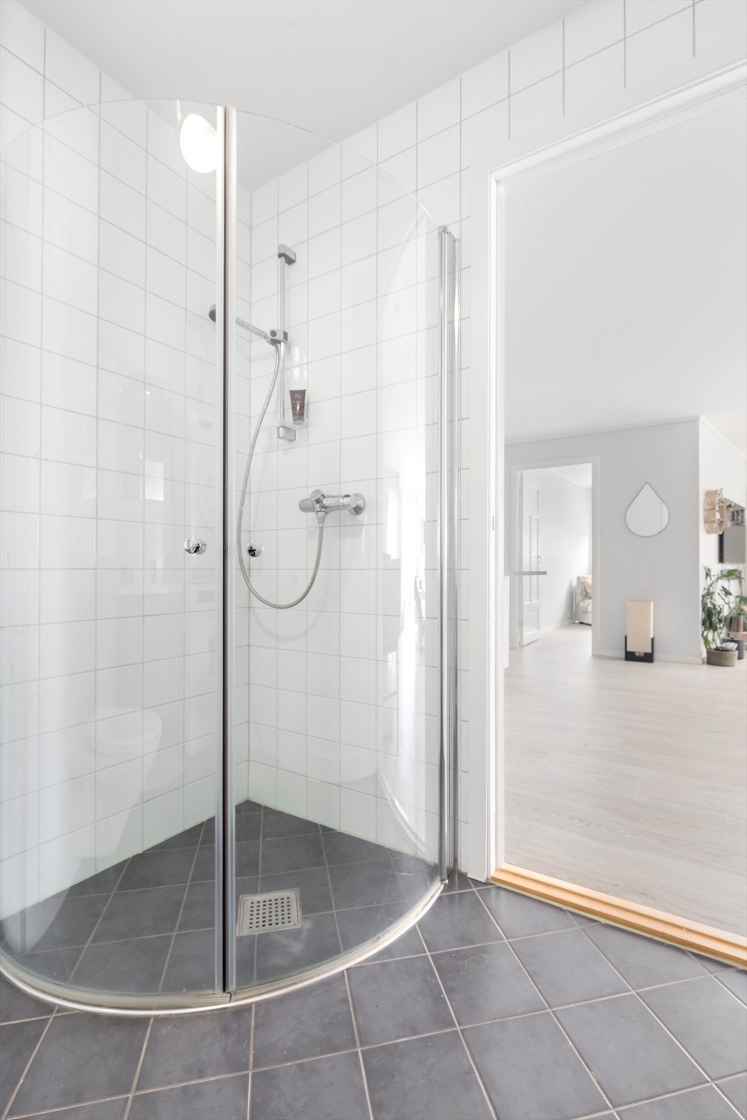 Bad/vaskerom har flislagte vegger og flislagte gulv med vannbåren varme | rommet er utstyrt med dusjhjørne med buede glassdører, vegghengt wc, baderomsinnredning og opplegg for vaskemaskin og tørketrommel Galleribilde