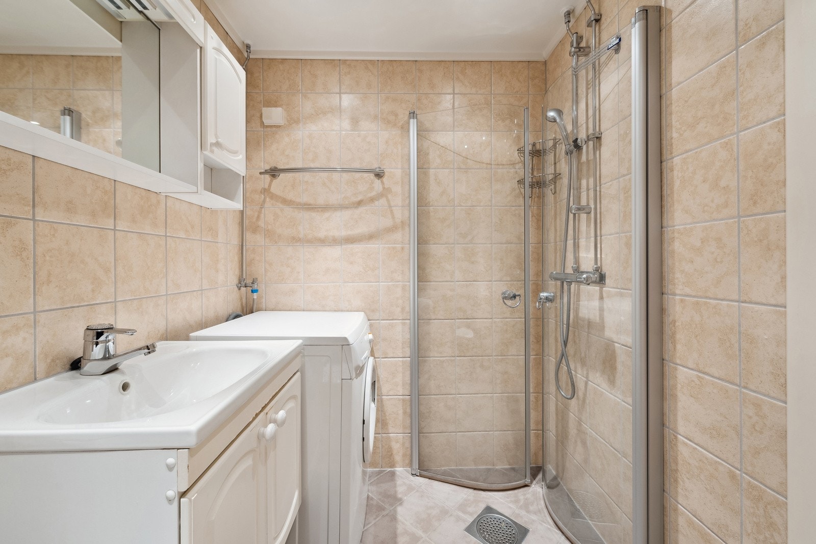 Badet har flislagte gulv med varme og downlights i tak. Badet består av speilskap med overlys og stikkontakt over servant, dusjhjørne med dører, vegghengt dusjarmatur og gulvstående toalett. Galleribilde