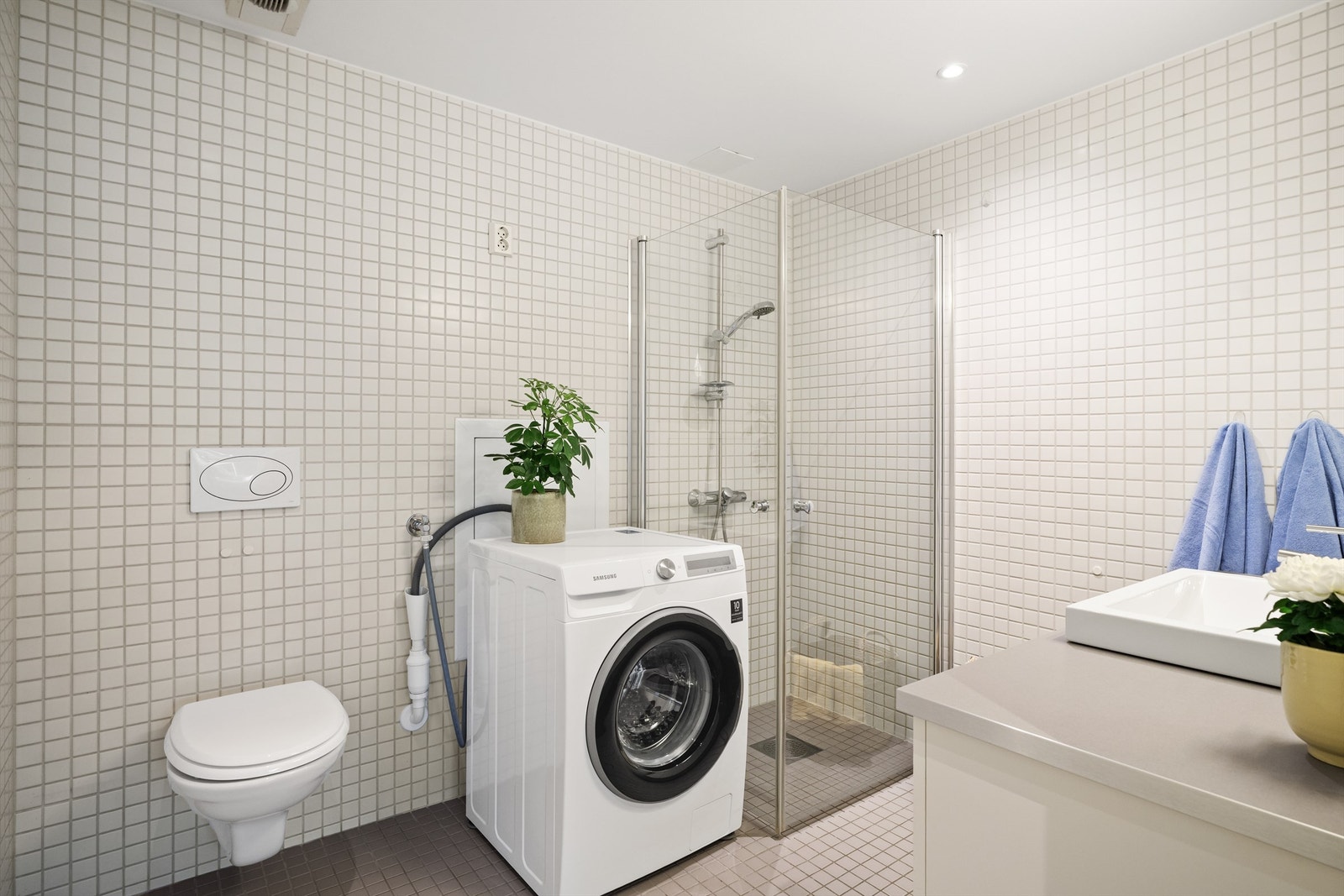 Innredningen består av vegghengt toalett, servant på innredning og dusjhjørne med svingbare glassdører. Galleribilde