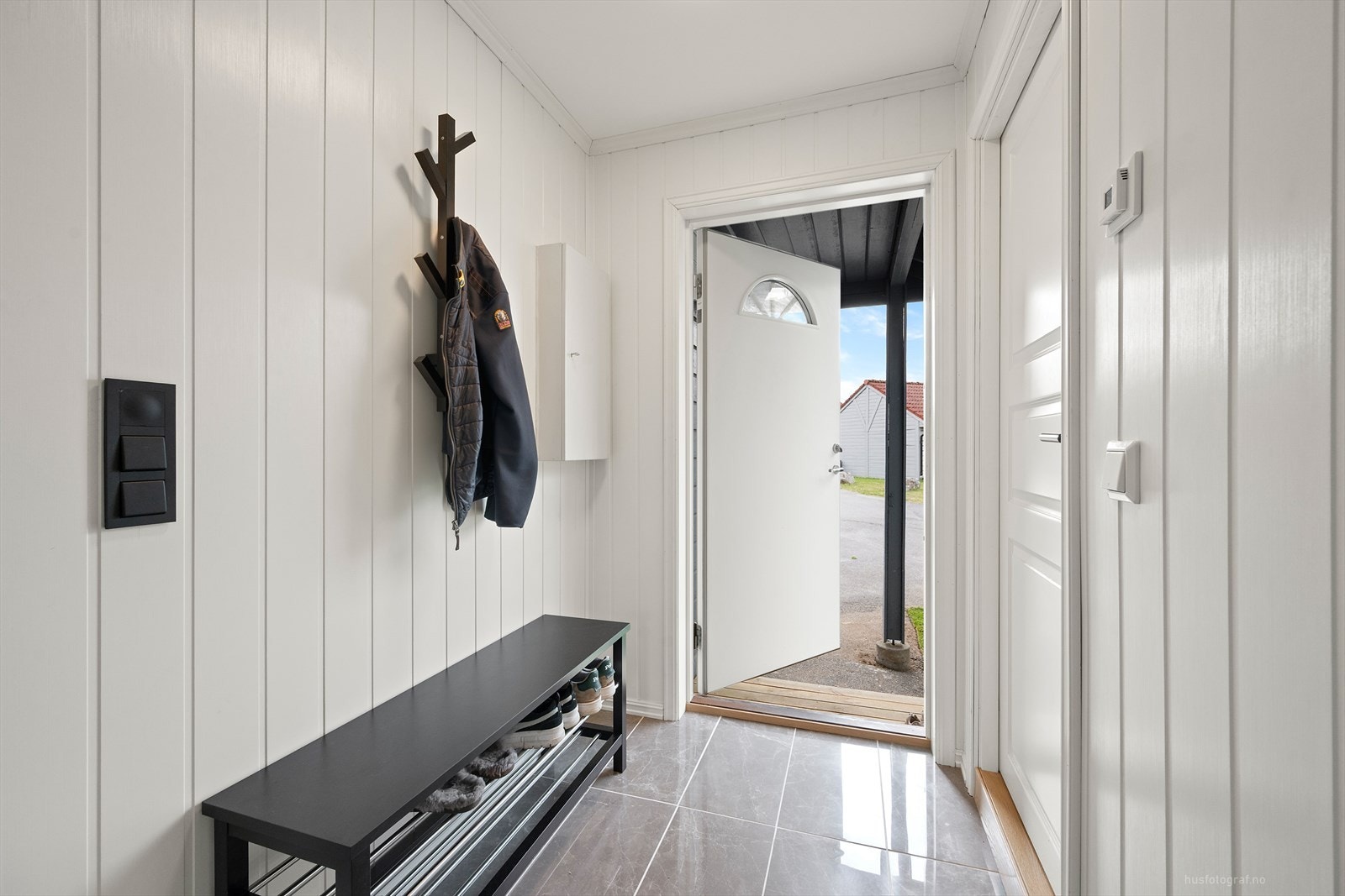 Velkommen inn i til en gang med fliser og plass til å henge fra seg ytterklær, det er inngang til badet fra gangen. Galleribilde