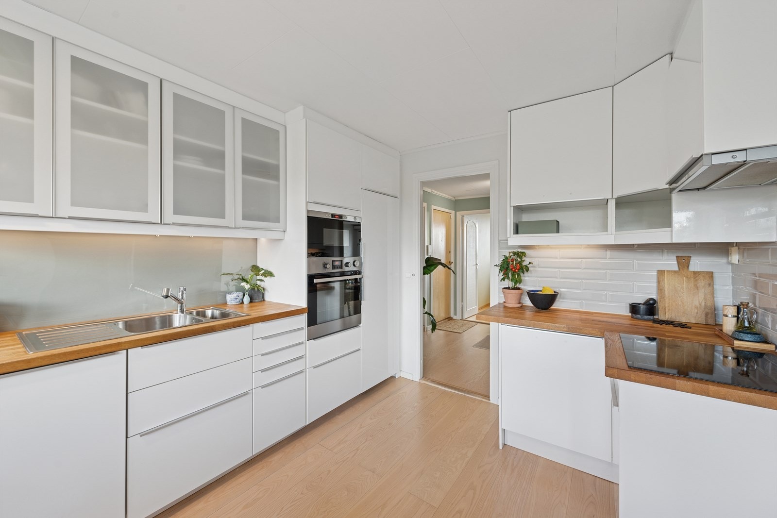 Innredning med hvite glatte fronter, heltre benkeplate, overskap med frostet glass, fliser og plater mellom benk og overskap. Galleribilde