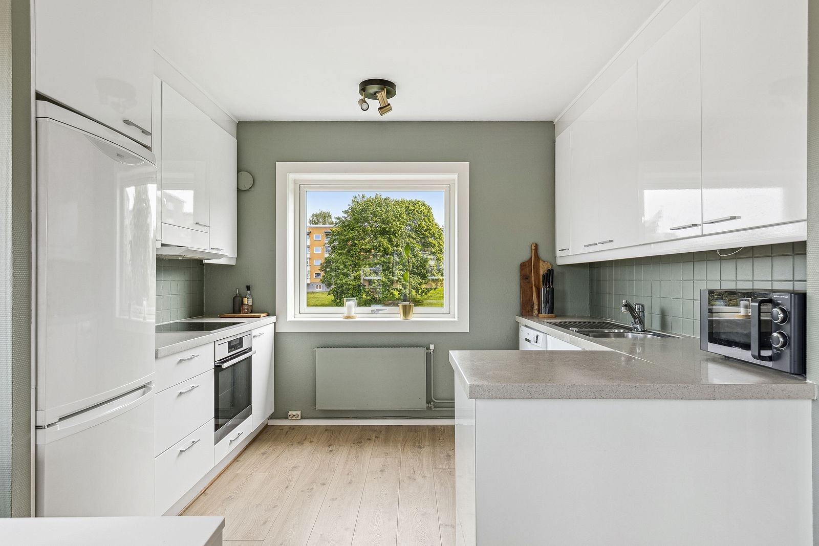 Pent kjøkken med hvite monderne fronter og hvitevarer. Galleribilde