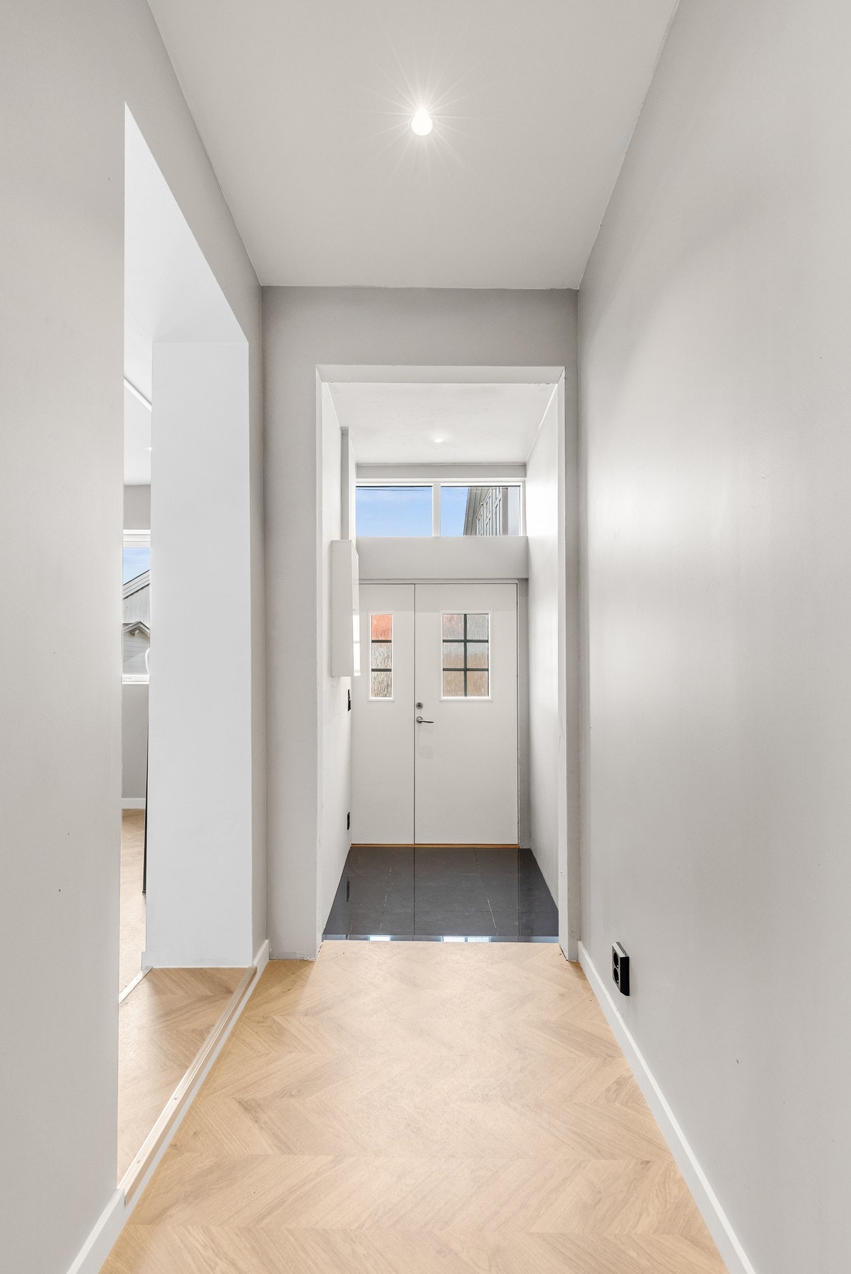 Lys entré/gang med både fliser og fiskebensparkett på gulv og slette flater på vegger og i himling Galleribilde