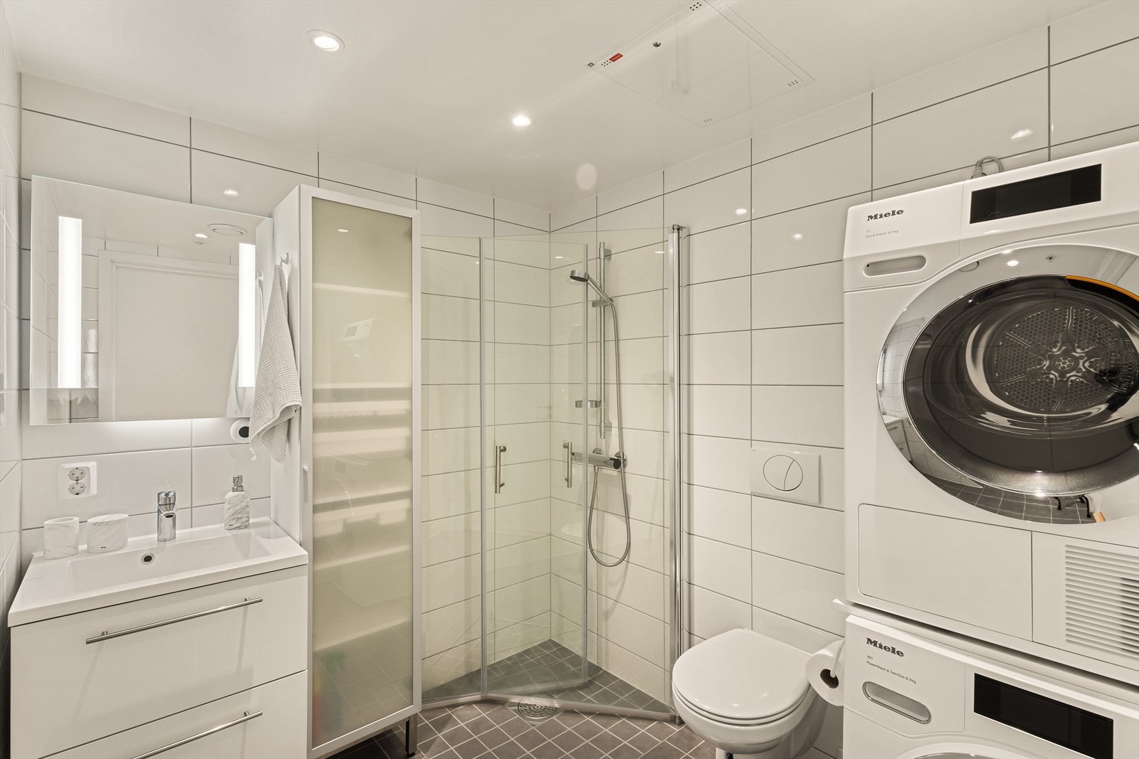 Badet er innredet med servant med møblement og speil, vegghengt toalett, innfeltbart dusjhjørne og opplegg for vaskemaskin. Galleribilde