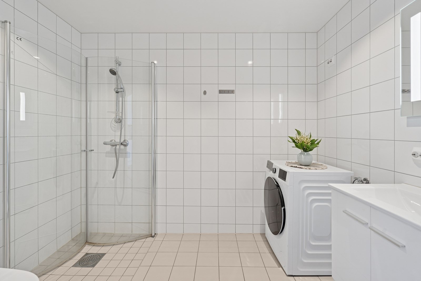 Vegghengt toalett, opplegg for vaskemaskin og belyst speilskap. For øvrig byr badet på en innbydende og romslig dusjsone med innfellbare glassdører. Galleribilde