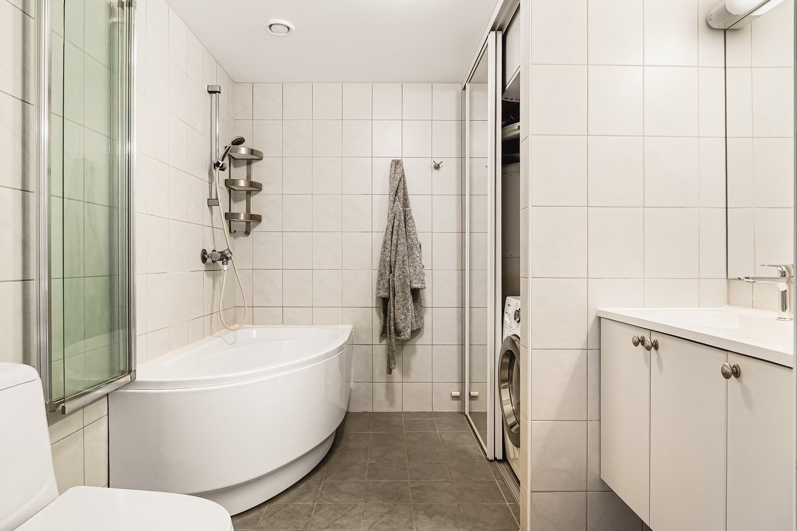 Badet er lyst og stilrent, med en praktisk skyvedør som skjuler opplegg for vaskemaskin og tørketrommel. Galleribilde