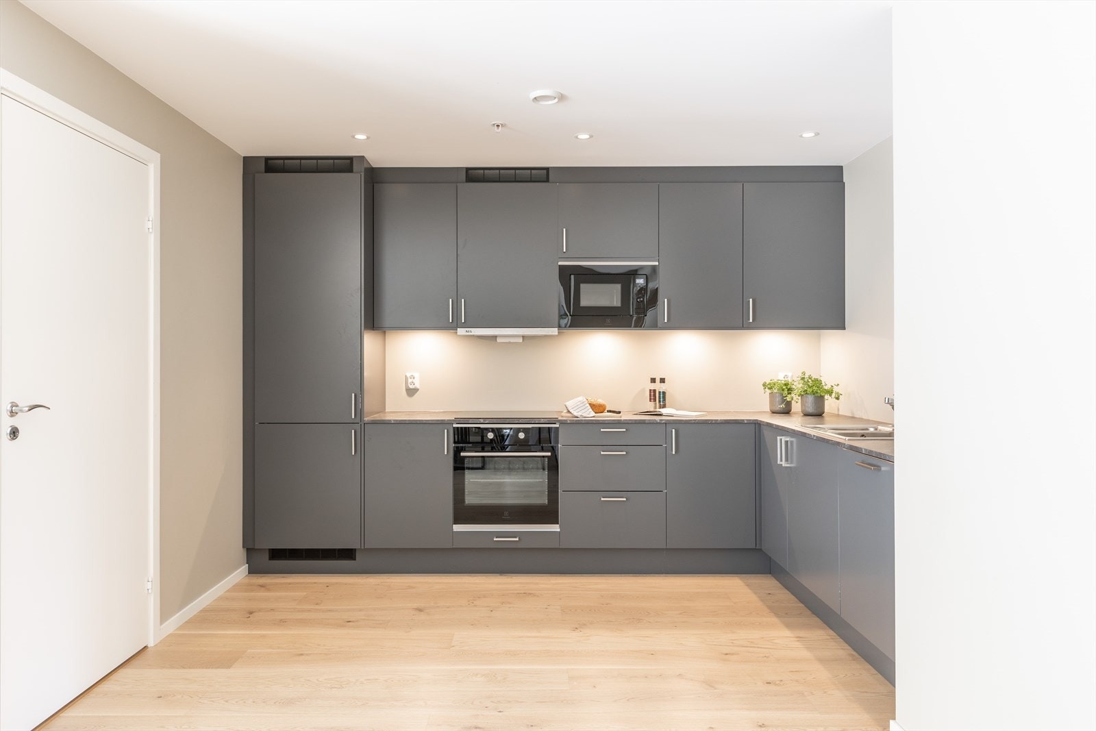 Flott og moderne takhøy kjøkkeninnredning fra Sigdal utført med slette fronter i en moderne gråfarge og benkeplate av laminat med nedfelt vask. Galleribilde