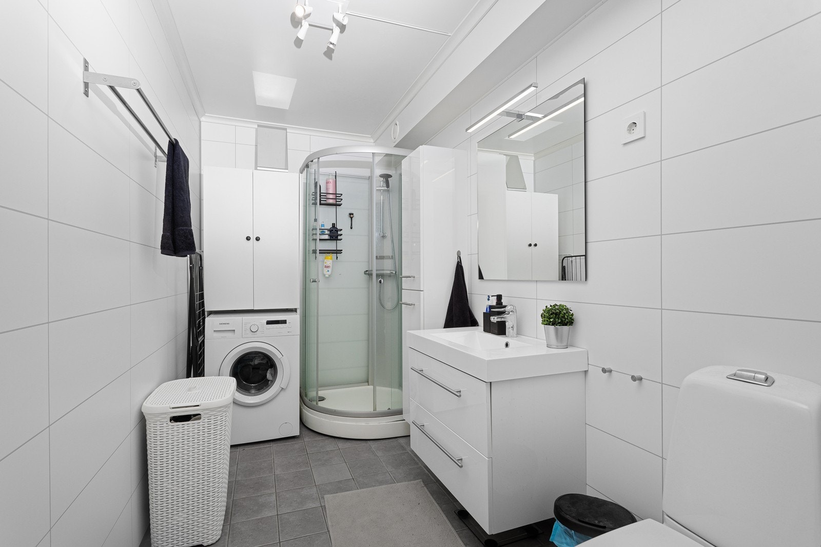 Badet i leiligheten er flislagt og har innredning med heldekkende servant, dusjkabinett, toalett og opplegg for vaskemaskin. Galleribilde