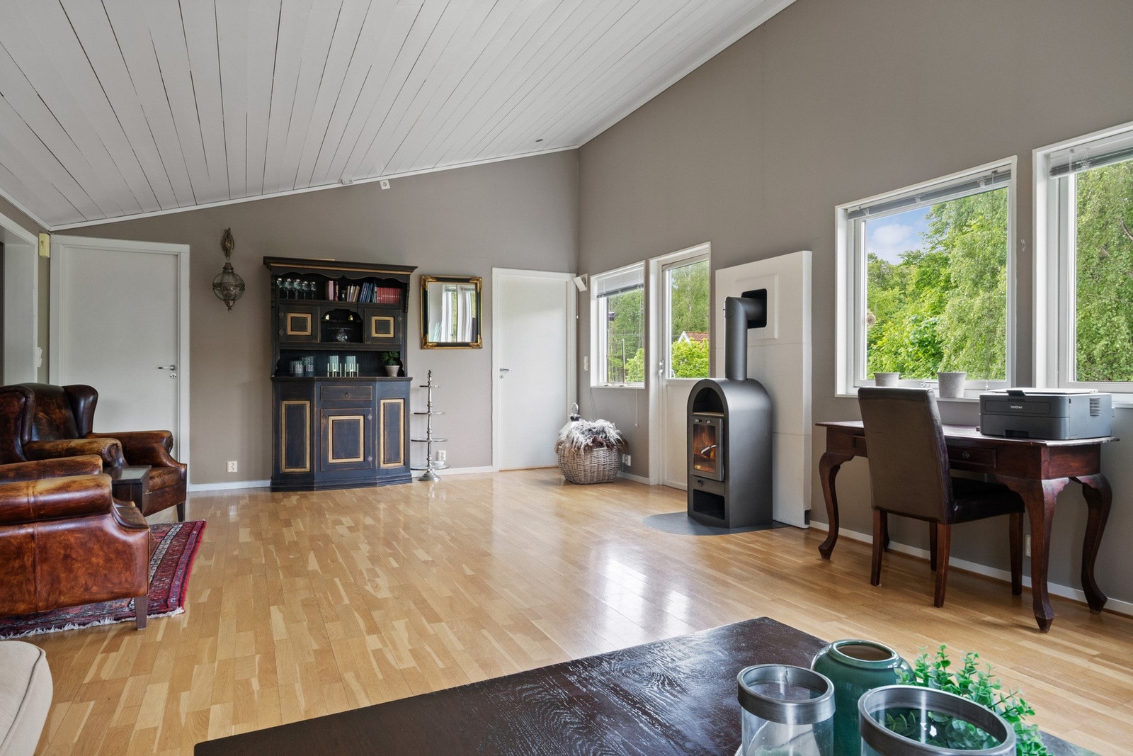 Stuen har parkettgulv, gråmalte, glatte veggflater, himling i hvitmalt panel og en peisovn som bidrar til ekstra hygge. Galleribilde