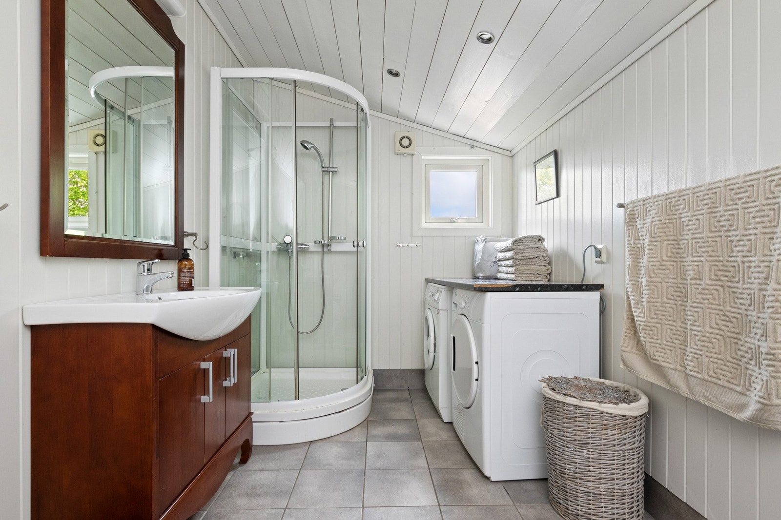 Badet i andre etasje har grå fliser på gulvet, hvitmalte veggflater i panel, hvitmalt skråtak i panel, downlights, et lite vindu og vannbåren gulvvarme. Galleribilde